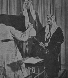 خير الدين الزركلي واقفاً خلف الملك سعود بن عبد العزيز في إحدى حواراته التلفزيونية.